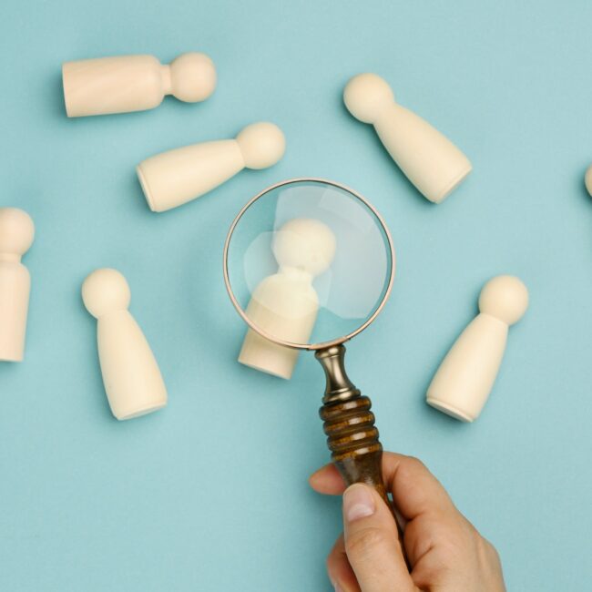 Wooden men and a magnifying glass on a blue background. Recruitment concept