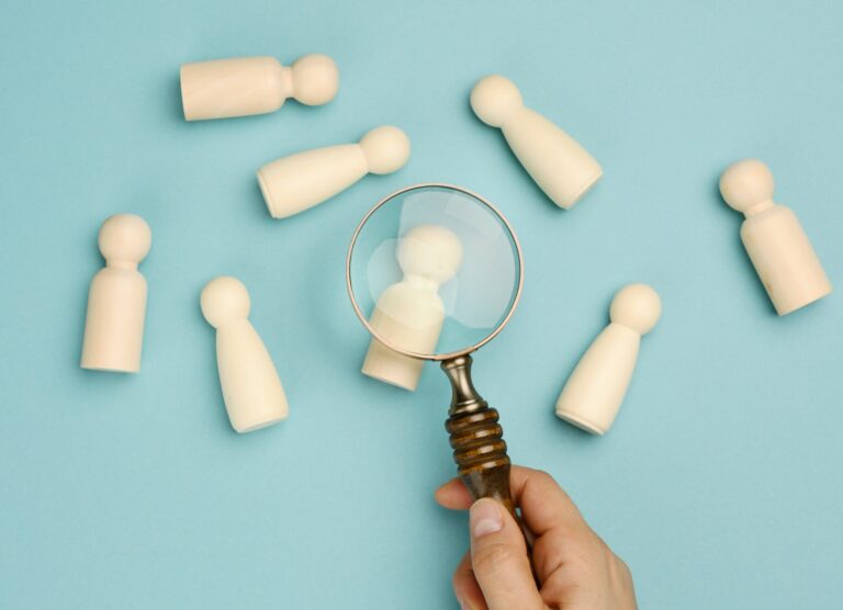 Wooden men and a magnifying glass on a blue background. Recruitment concept